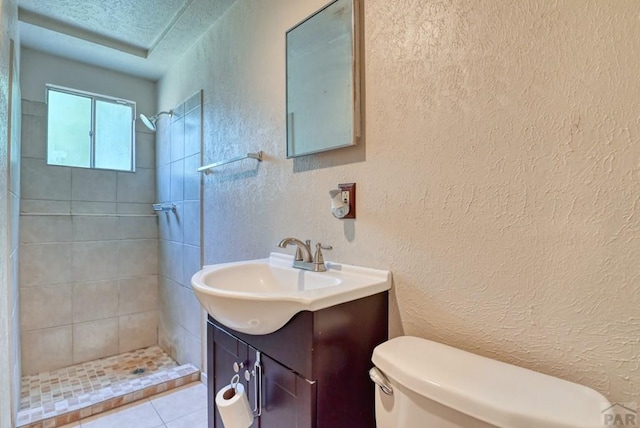 bathroom featuring a textured ceiling, a textured wall, toilet, vanity, and tiled shower