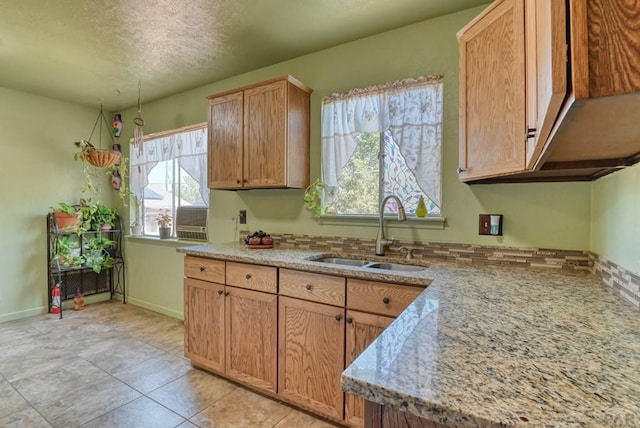 kitchen featuring light tile patterned floors, baseboards, light stone countertops, a textured ceiling, and a sink