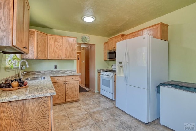 kitchen featuring light tile patterned floors, white appliances, a sink, and light stone counters