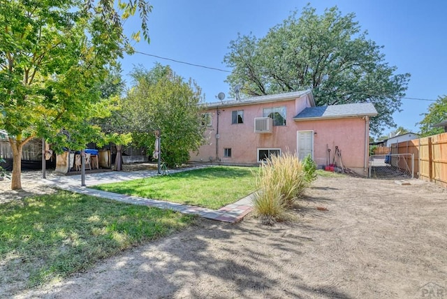 rear view of house with a wall unit AC, a yard, a fenced backyard, and stucco siding