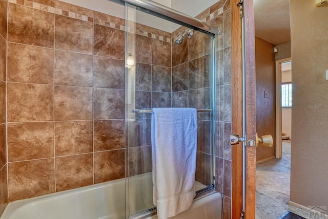 bathroom with combined bath / shower with glass door and a textured wall