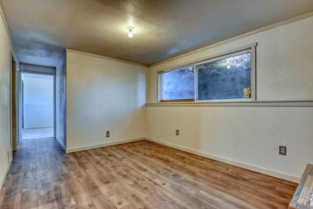 spare room featuring a textured ceiling, light wood-type flooring, and baseboards