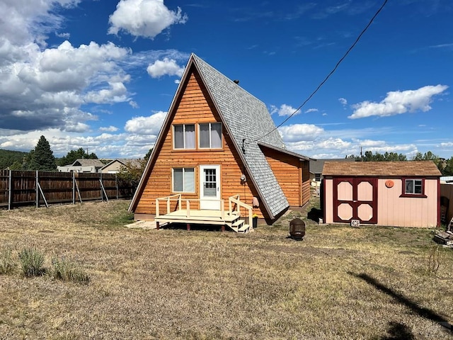 rear view of property with a yard, a shingled roof, fence, a shed, and an outdoor structure