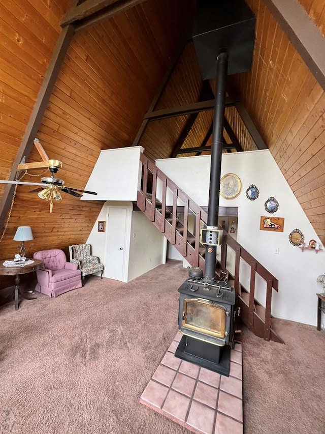 living area with beamed ceiling, carpet, and a wood stove