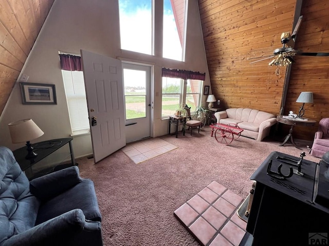 living room with ceiling fan, high vaulted ceiling, light colored carpet, and wooden walls