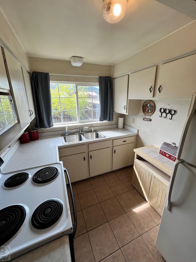 kitchen with light tile patterned floors, freestanding refrigerator, a sink, light countertops, and white range with electric cooktop