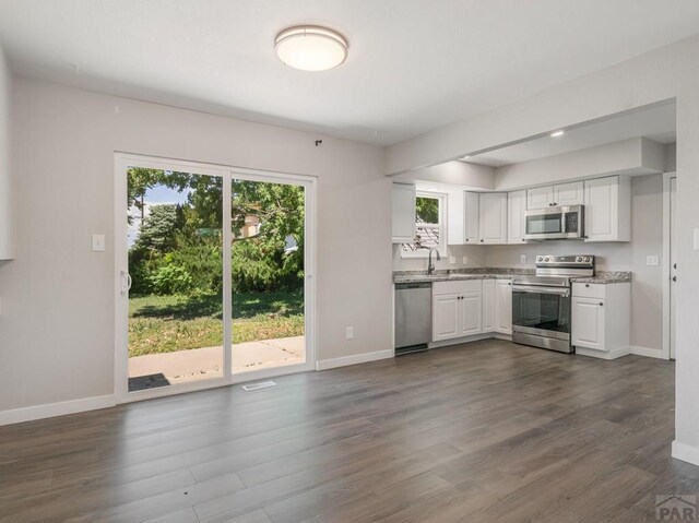 kitchen with dark wood-style floors, stainless steel appliances, baseboards, and white cabinets