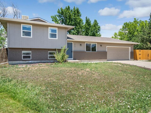 split level home featuring brick siding, concrete driveway, an attached garage, a front yard, and fence