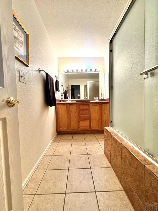 4147 Outlook Blvd Unit F, Pueblo, CO 81008 - bathroom with vanity, baseboards, tile patterned flooring, a textured ceiling, and a shower with shower door
