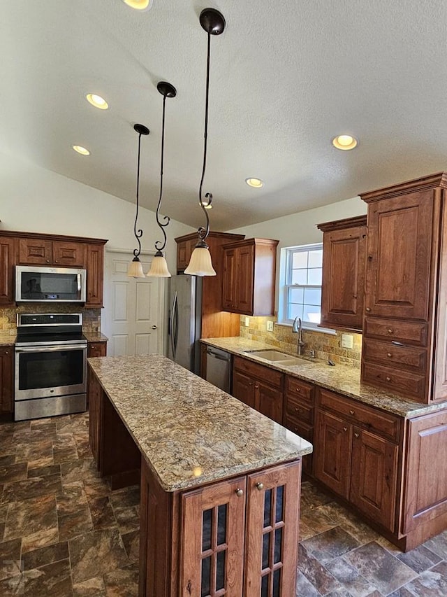 kitchen featuring pendant lighting, stainless steel appliances, stone finish floor, a kitchen island, and a sink