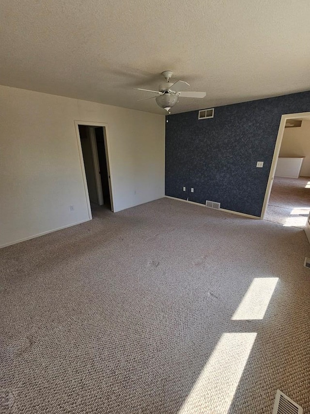 spare room with carpet floors, a ceiling fan, visible vents, and a textured ceiling