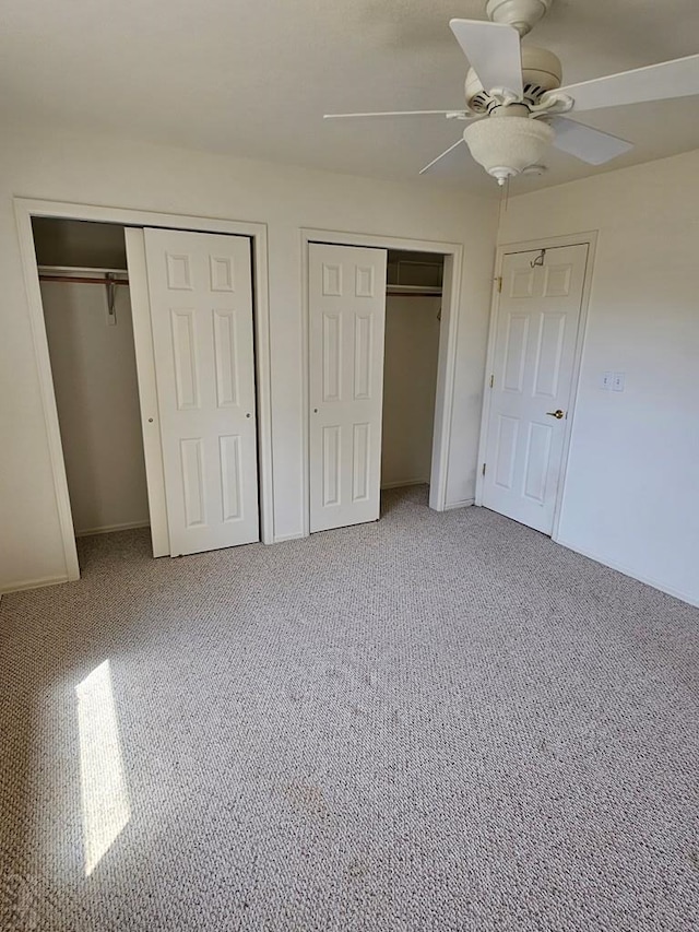 unfurnished bedroom with carpet floors, ceiling fan, and two closets