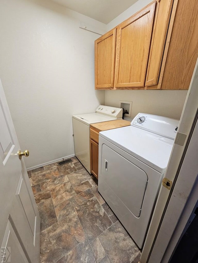 laundry room featuring stone finish floor, cabinet space, independent washer and dryer, and baseboards