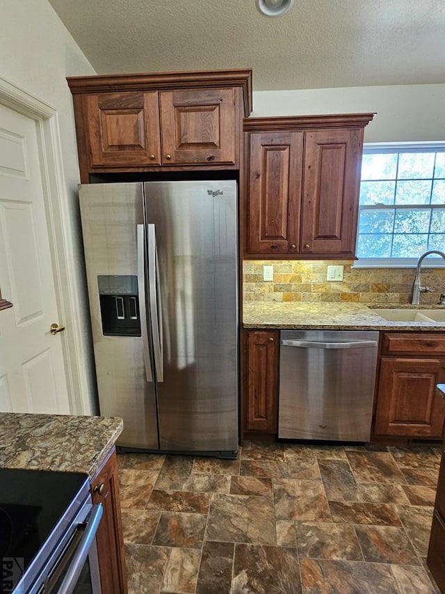 kitchen with light stone counters, a sink, appliances with stainless steel finishes, decorative backsplash, and stone finish flooring