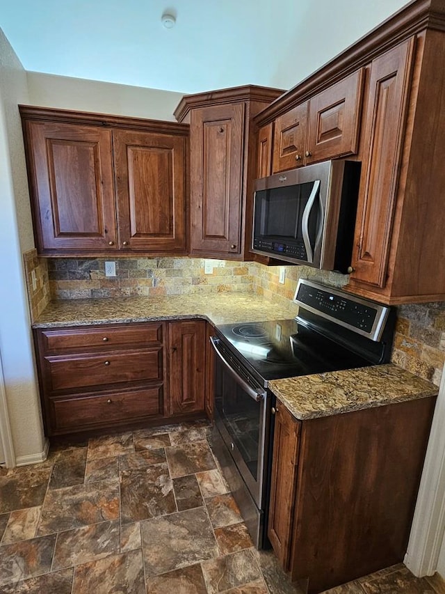 kitchen featuring appliances with stainless steel finishes, stone finish floor, decorative backsplash, and light stone countertops