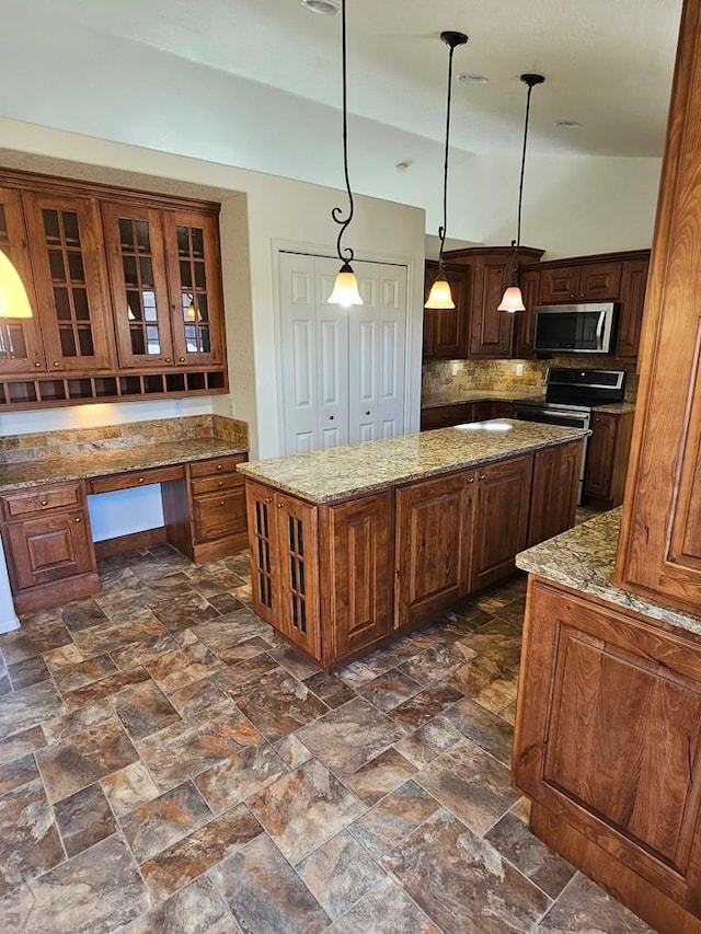 kitchen featuring a center island, pendant lighting, built in desk, appliances with stainless steel finishes, and glass insert cabinets