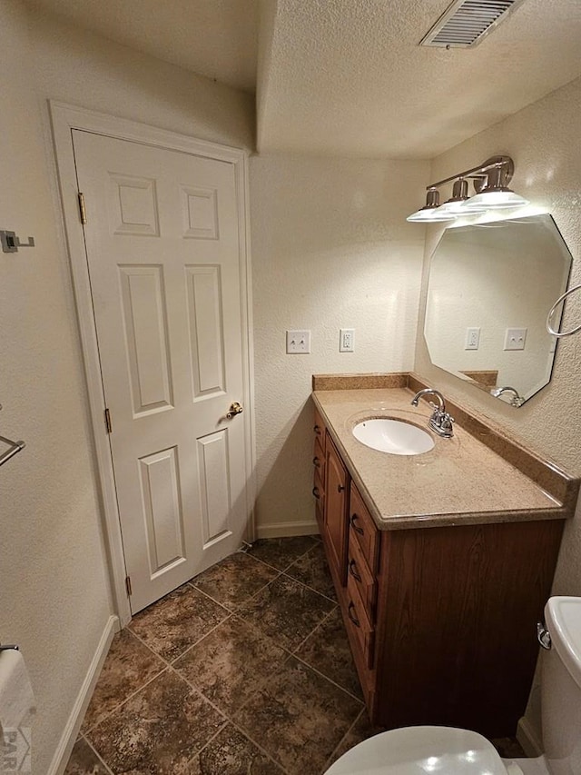 half bath with a textured ceiling, toilet, vanity, visible vents, and baseboards