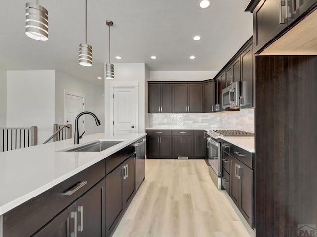 kitchen featuring stainless steel appliances, a sink, dark brown cabinets, light countertops, and pendant lighting