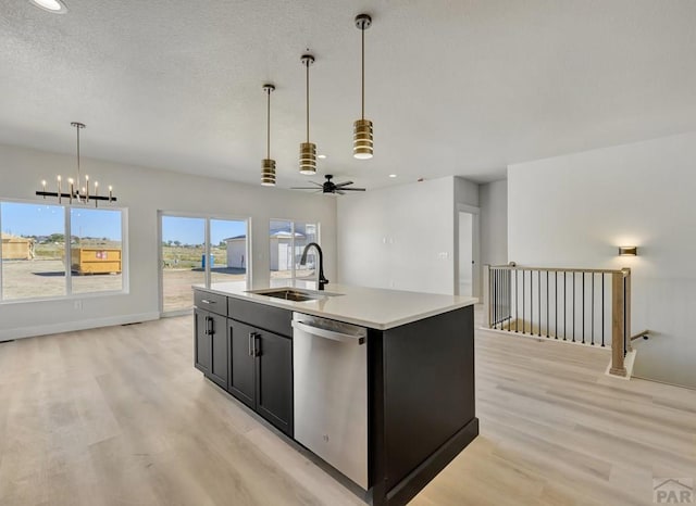 kitchen with a kitchen island with sink, light countertops, stainless steel dishwasher, pendant lighting, and a sink