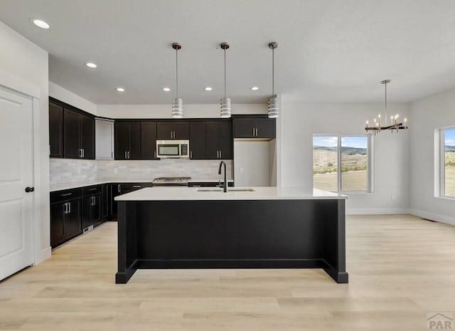 kitchen featuring appliances with stainless steel finishes, decorative light fixtures, a kitchen island with sink, light countertops, and a sink