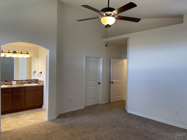 unfurnished bedroom with baseboards, high vaulted ceiling, a sink, and light colored carpet