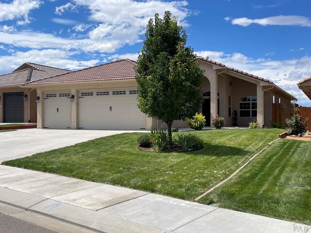 view of front facade featuring a garage, a tiled roof, a front lawn, and stucco siding