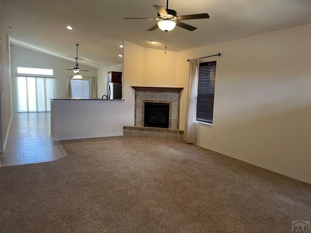 unfurnished living room featuring light carpet, vaulted ceiling, a tile fireplace, and a ceiling fan