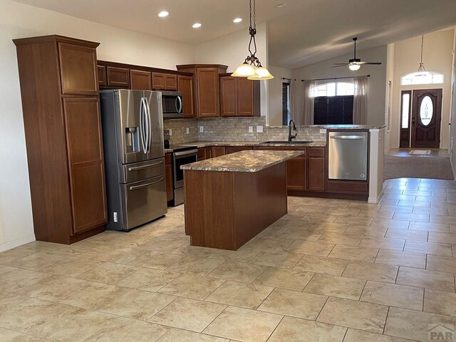 kitchen with stainless steel appliances, a peninsula, a sink, dark stone countertops, and decorative light fixtures