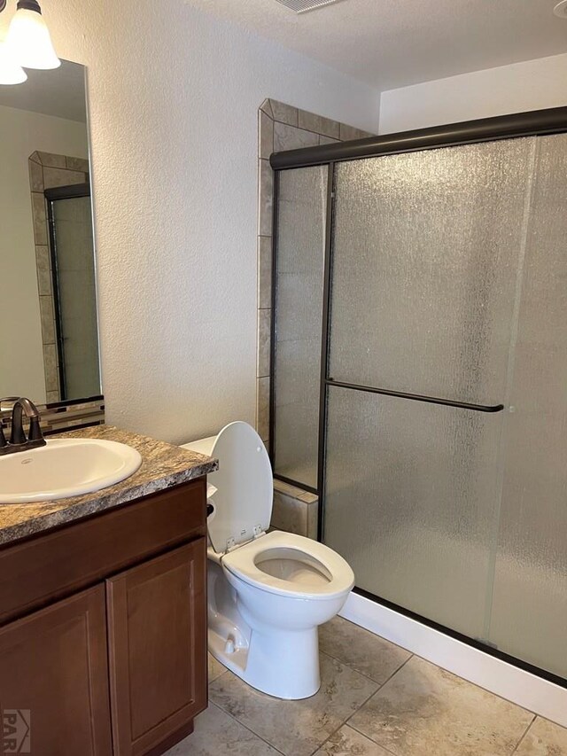 bathroom with toilet, a textured wall, a shower stall, and vanity