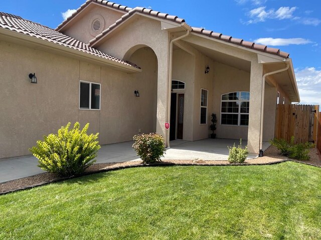 exterior space with fence, a tile roof, a lawn, stucco siding, and a patio area