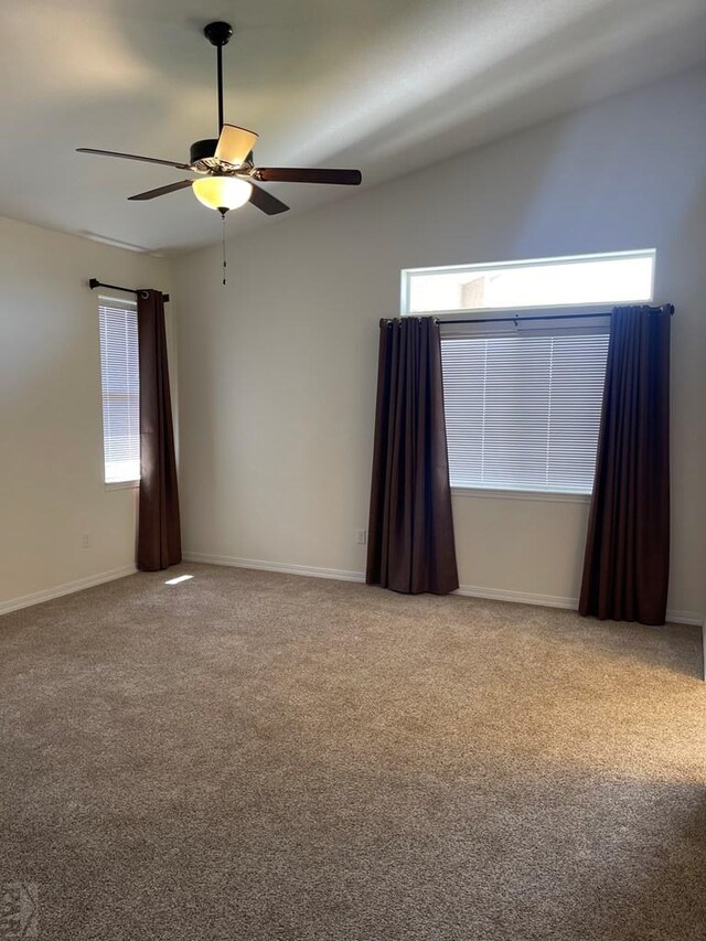 empty room featuring light carpet, vaulted ceiling, a ceiling fan, and baseboards