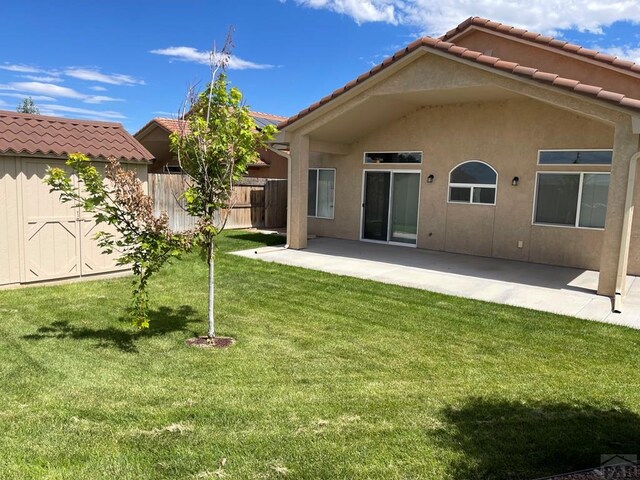 rear view of house with a yard, a patio, stucco siding, fence, and a tiled roof