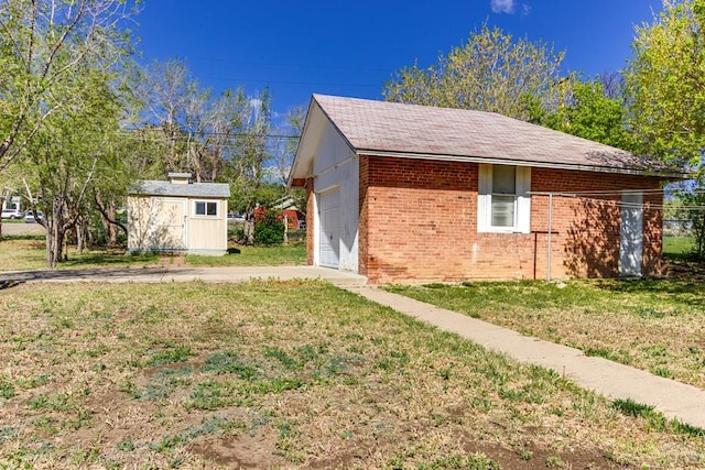 view of side of property featuring an outdoor structure, a garage, driveway, brick siding, and a yard