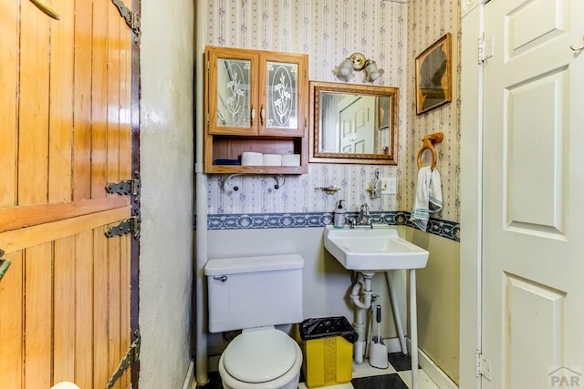 half bath featuring toilet, wallpapered walls, and a sink