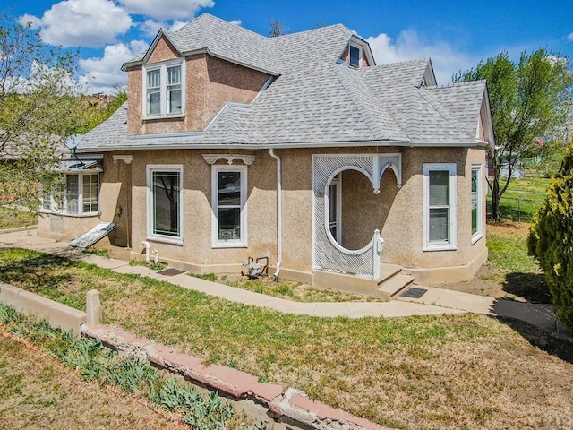 view of front of home featuring fence, a shingled roof, stucco siding, and a front yard