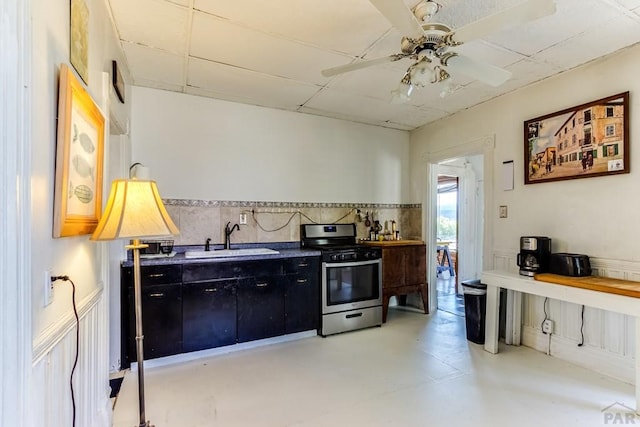 kitchen featuring wainscoting, concrete flooring, dark cabinets, stainless steel range with gas stovetop, and a sink