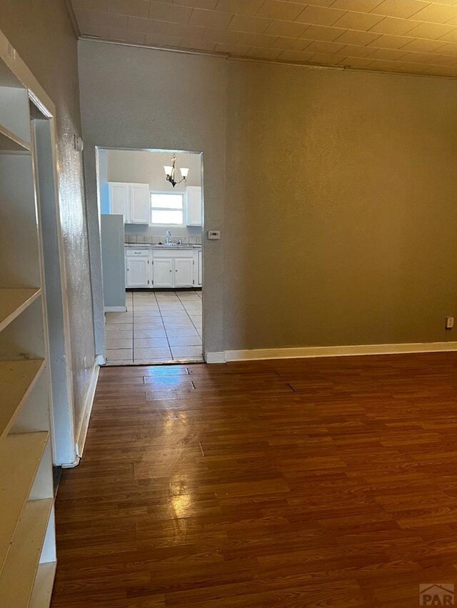 spare room featuring a sink, a notable chandelier, baseboards, and wood finished floors