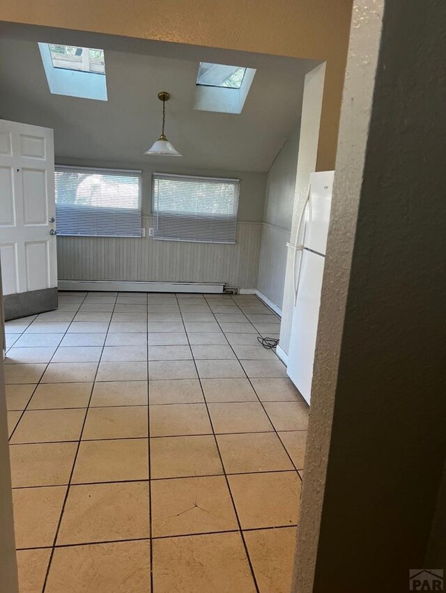 empty room with a baseboard heating unit, vaulted ceiling with skylight, wainscoting, and light tile patterned flooring