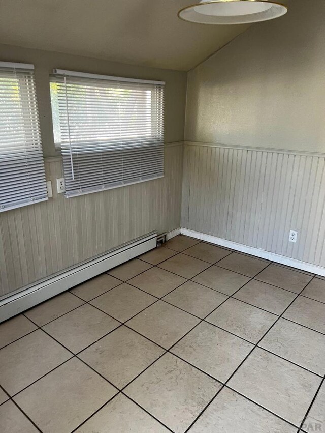 unfurnished room featuring a wainscoted wall, a baseboard radiator, tile patterned floors, and a healthy amount of sunlight