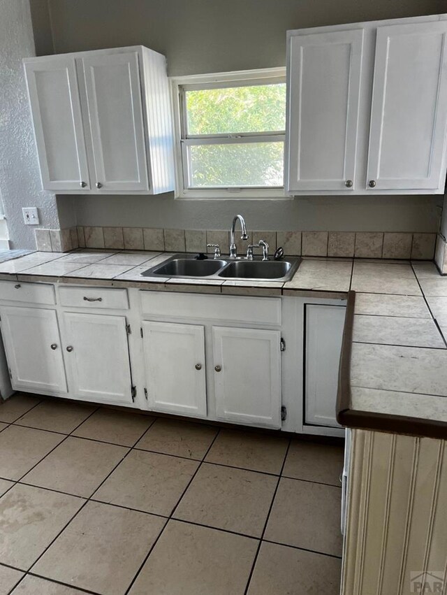 kitchen with white cabinets, a sink, tile countertops, and light tile patterned floors