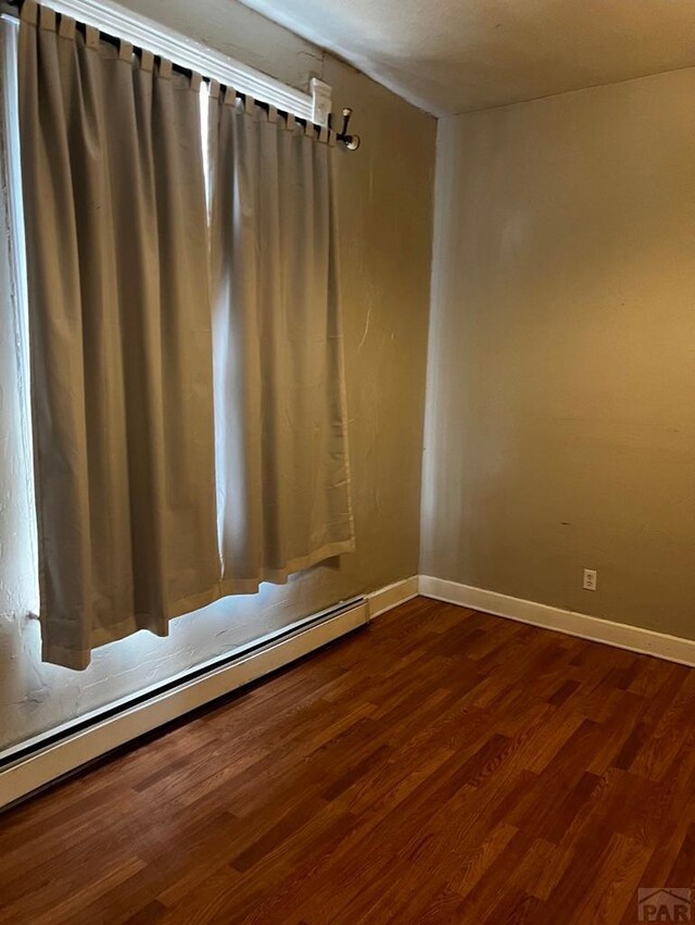 spare room featuring a baseboard radiator, dark wood-style flooring, and baseboards