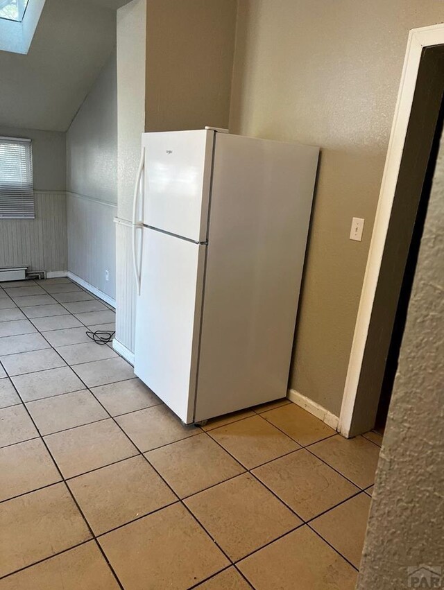 kitchen with a wainscoted wall, lofted ceiling with skylight, light tile patterned flooring, and freestanding refrigerator