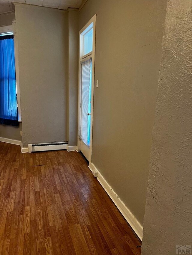 spare room with baseboard heating, wood finished floors, and baseboards