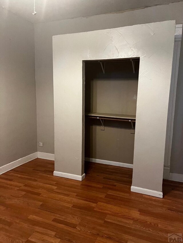 unfurnished bedroom with dark wood-type flooring, a closet, and baseboards