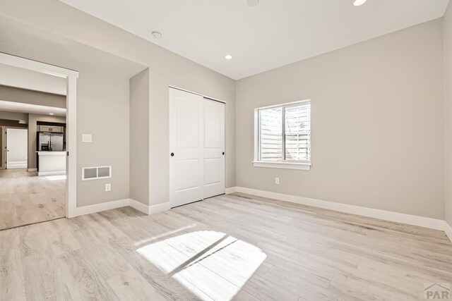 unfurnished bedroom featuring light wood-type flooring, stainless steel fridge, visible vents, and baseboards