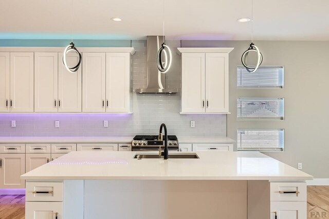 kitchen featuring a kitchen island with sink, wall chimney exhaust hood, and decorative light fixtures