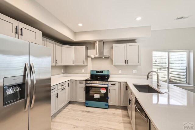 kitchen with wall chimney range hood, appliances with stainless steel finishes, light countertops, and a sink