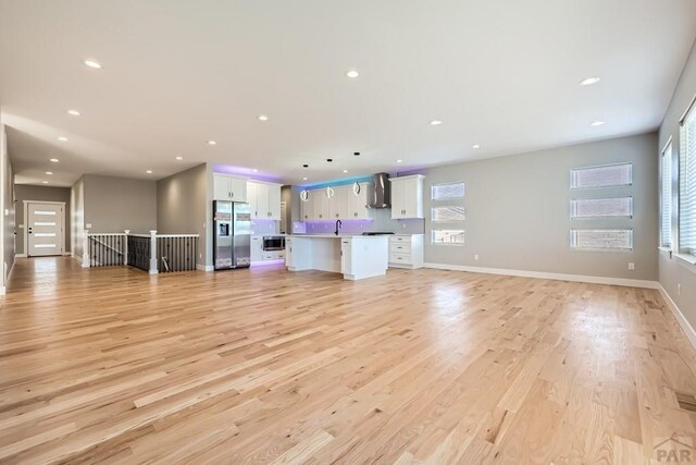 unfurnished living room with light wood finished floors, baseboards, a sink, and recessed lighting