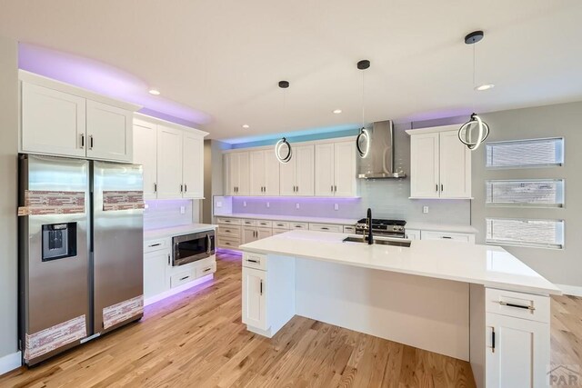 kitchen with stainless steel appliances, light countertops, decorative light fixtures, and wall chimney exhaust hood