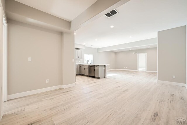 unfurnished living room featuring light wood finished floors, baseboards, visible vents, a sink, and recessed lighting